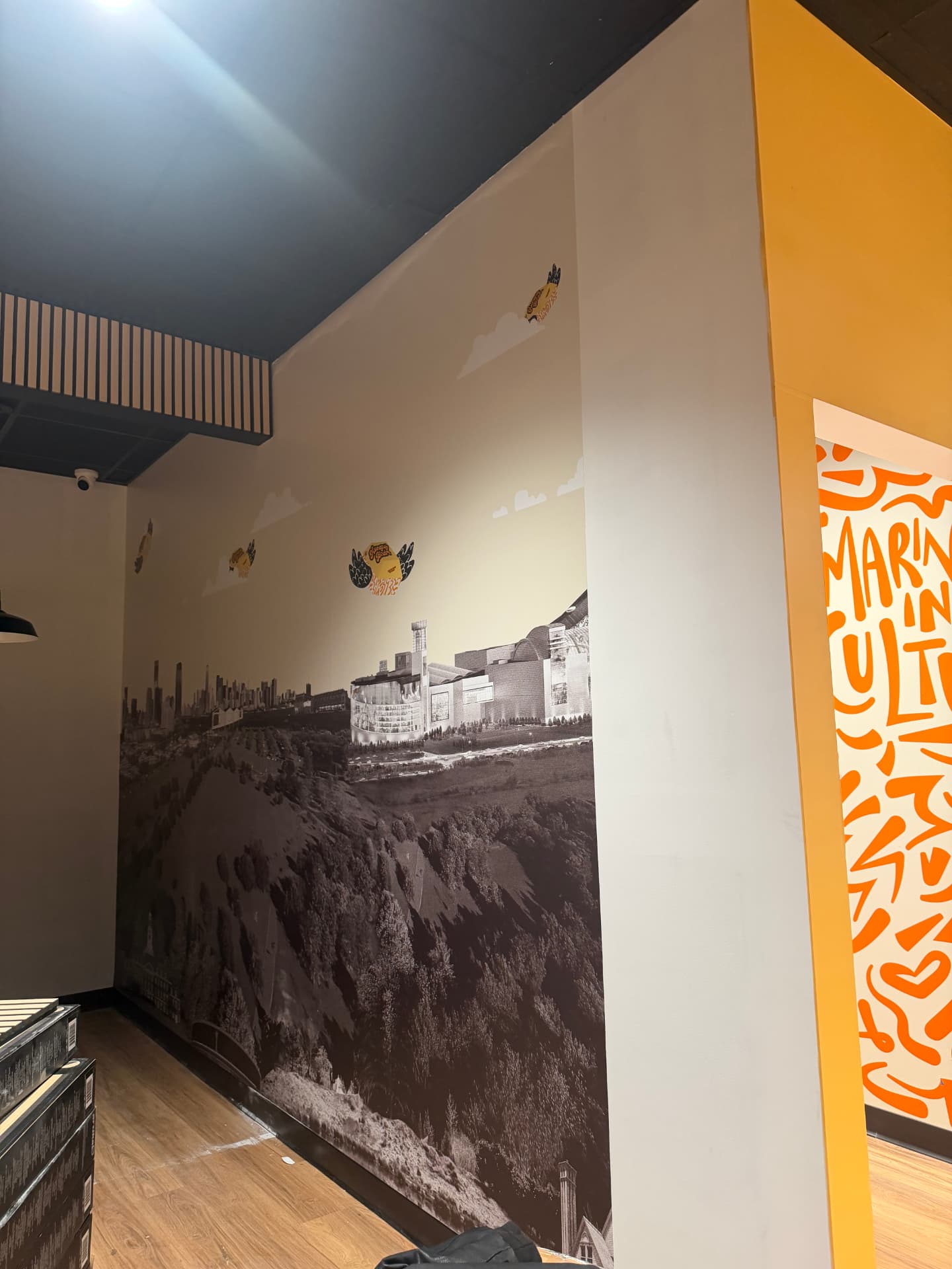 Full-height wall mural with illustrated cityscape and brand badges in a retail stairwell