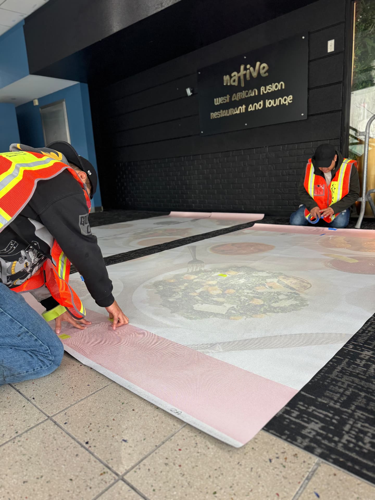 Crew installing a large format Native restaurant wall graphic on black brick