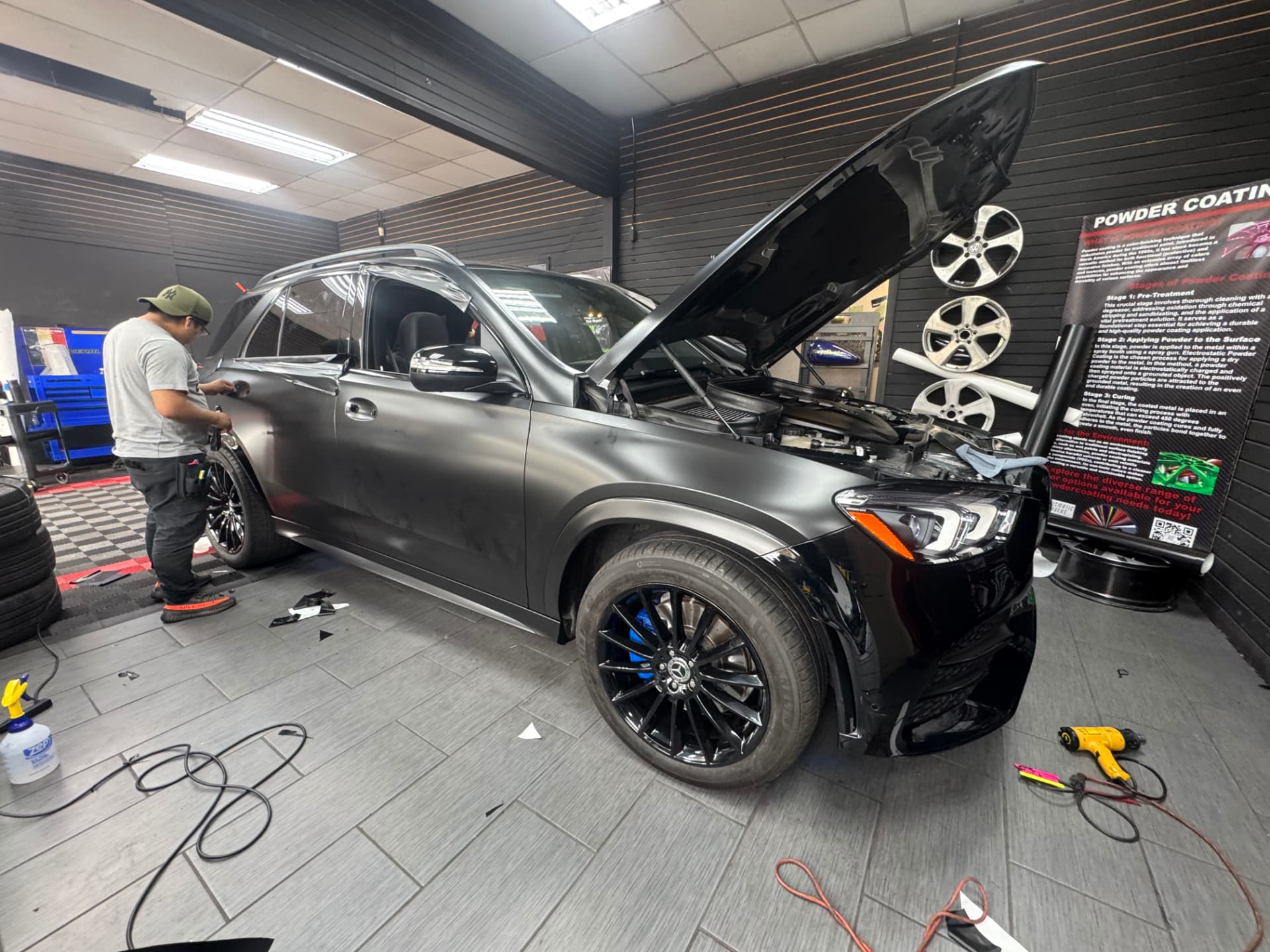 Installer squeegeeing satin black film onto a Mercedes GLE in the shop